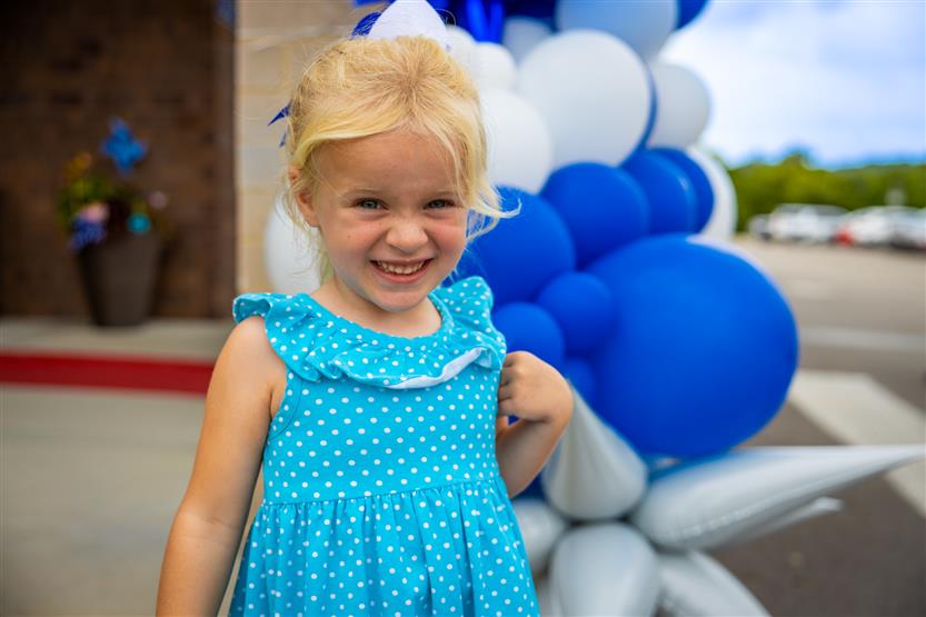 A little girl wearing a blue dress smiles